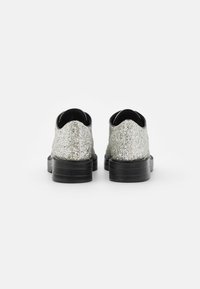 Silver glitter snörskor med rund tå, svarta sulor och texturerad detalj på baksidan. Enkel design med platt klack.