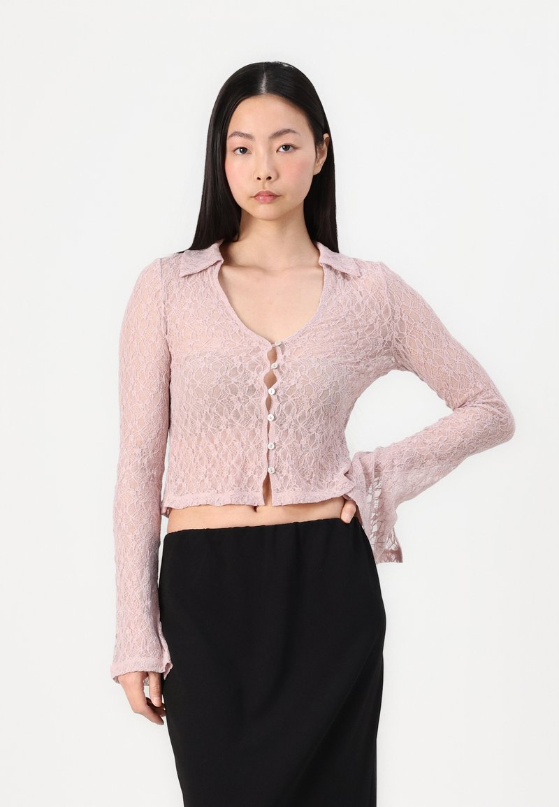 Cardigan in pizzo rosa chiaro con colletto, maniche lunghe e chiusure a bottone; design corto con orlo ondulato e trama intricata.
