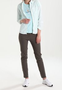 Camicia azzurro chiaro sopra una t-shirt grafica azzurro chiaro, abbinata a pantaloni marroni e sneakers bianche. La camicia ha una tasca e un tessuto strutturato.