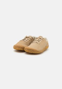 Zapatillas deportivas beige con parte superior de cuero suave, suela de goma texturizada y cordones contrastantes. Presentan un diseño de perfil bajo y una tracción robusta.