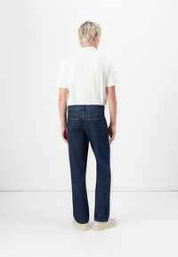 Camisa blanca de manga corta combinada con jeans de denim azul oscuro. Los jeans tienen un corte recto y bolsillos traseros clásicos, llevados con zapatillas claras.