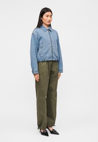 Τζιν μπουφάν με φερμουάρ μπροστά, γιακά και πλαϊνές τσέπες, συνδυασμένο με παντελόνι ελιάς και μαύρες γόβες με μυτερή μύτη.