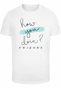 Camiseta blanca de algodón con la frase "¿cómo te va?" en cursiva negra y "F.R.I.E.N.D.S" en negrita, con un acento de pincelada azul.