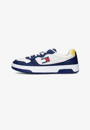 Sneakers bianchi in pelle con accenti blu navy, dotati di una toppa con logo blu e rosso, accentuazione gialla sul tallone e lacci bianchi, progettati per l'uso casual.