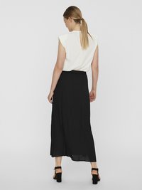 Haut sans manches blanc avec une fente à l'arrière, associé à une longue jupe noire. La jupe présente une coupe ample et une taille élastique. Sandales noires à talons carrés.
