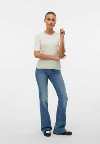 Top de punto crema con relieve y mangas cortas, combinado con jeans de campana de color azul claro y zapatos negros con acentos blancos. Diseño simple y ajustado.