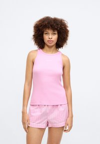 Ροζ ριμπ μπουστάκι με στρογγυλή λαιμόκοψη και branding Calvin Klein. Συνδυάζεται με ανοιχτό ροζ σορτσάκια με ρίγες και λεπτομέρεια στο στρίφωμα.