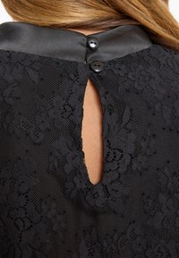 Black dress featuring a textured lace overlay, satin collar, and a keyhole cutout at the back secured with two black buttons.