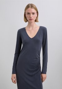 Vestido de manga larga en tejido gris oscuro, con escote en V y detalle de fruncido lateral, textura lisa y silueta ajustada.