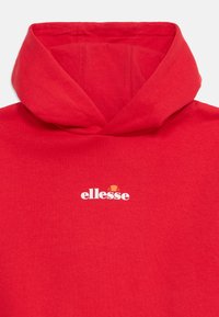 Červená mikina s kapucňou, na prednej strane s logom "ellesse" napísaným bielymi písmenami, nad textom je oranžový a červený polkruh.