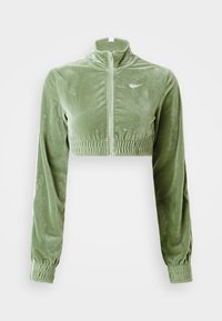 Chaqueta corta de terciopelo verde con alto cuello, cierre de cremallera, dobladillo elástico y mangas. Presenta un logo sutil en el lado izquierdo del pecho.