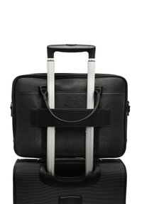 Sort kuffert på hjul med et sølvfarvet teleskophåndtag, struktureret overflade og en matchende laptoptaske, der er sikret til håndtaget med stropper.