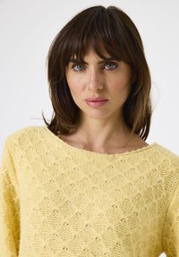 Geel gebreide trui met een losse, brede halslijn en een textuurpatroon met ruitvormen. Zacht, warm materiaal met een casual pasvorm.