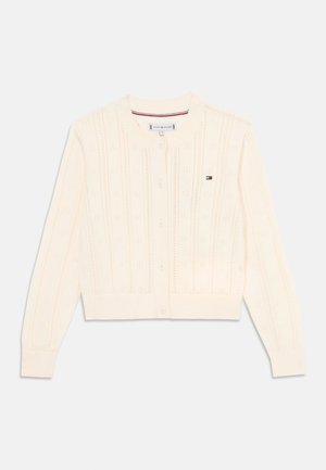 Strikket kremfarget cardigan med ribbestruktur, rund hals, seks knapper og en liten logo-detalj på brystet.