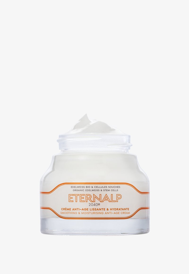 Durchsichtiger Glasbehälter mit einer weißen Creme darin. Das Etikett enthält orangene Schriftzüge und dekorative Elemente, auf denen "Eternalp" und Produktdetails angegeben sind.