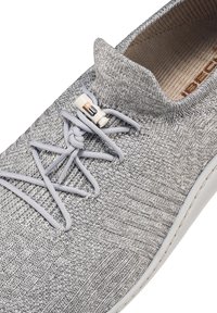 Jasnoszary dzianinowy but z zapięciem typu slip-on, teksturowanym materiałem, kontrastującą białą podeszwą oraz ozdobnym wiązaniem.