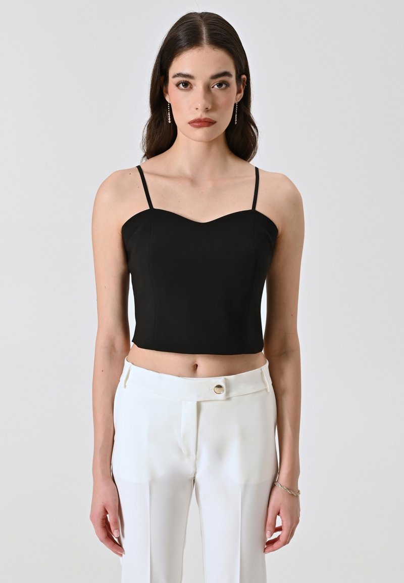 Zwarte crop top met dunne banden, aansluitend ontwerp, gladde stof en sweetheart halslijn, gecombineerd met witte broeken met een knoop.