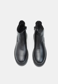 Un paio di stivaletti neri in pelle, con punta tonda e cerniere laterali, mostrati dall'alto su uno sfondo bianco.