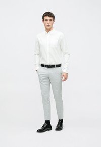 Valge nööpidega särk, hallikirju püksid, must vöö ja mustad kingad. Kitsas lõige koos rinnataskuga. Neutraalsete värvide palett.