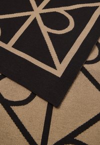 Detailný pohľad na preložené čierne a béžové tkaniny s prekrývajúcim sa geometrickým vzorom línií a kriviek.