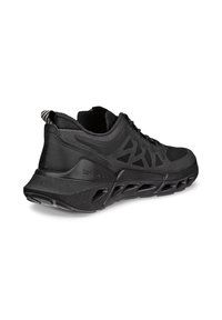 Chaussure de sport noire avec tige en mesh, motif géométrique latéral, semelle épaisse ventilée et languette à l’arrière, inclinée pour montrer le côté extérieur et le talon.