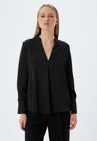 Sort langærmet bluse med V-hals og plissering. Fremstillet af glat stof med en afslappet pasform og fastsatte ærmer.