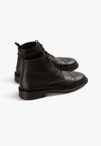 Botas de cuero negro hasta el tobillo con acabado texturizado, puntera redondeada, diseño con cordones y un tacón bajo apilado. Acabadas con costuras marrones.
