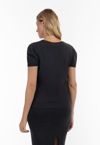 Sort kortærmet top i en tætsiddende design, med rund halsudskæring og ribbede manchetter. Glat tekstur uden synlige mønstre eller detaljer.