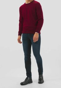 Maglione bordeaux a girocollo, jeans blu scuro slim-fit e scarpe nere con lacci e dettagli testurizzati. Design semplice, silhouette aderente.