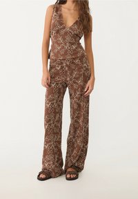 Brązowy kombinezon w kwiatowy wzór z głębokim dekoltem w kształcie V, luźnymi szerokimi nogawkami i wyszywanymi białymi kwiatami. Wykonany z lekkiego materiału, o swobodnym kroju.