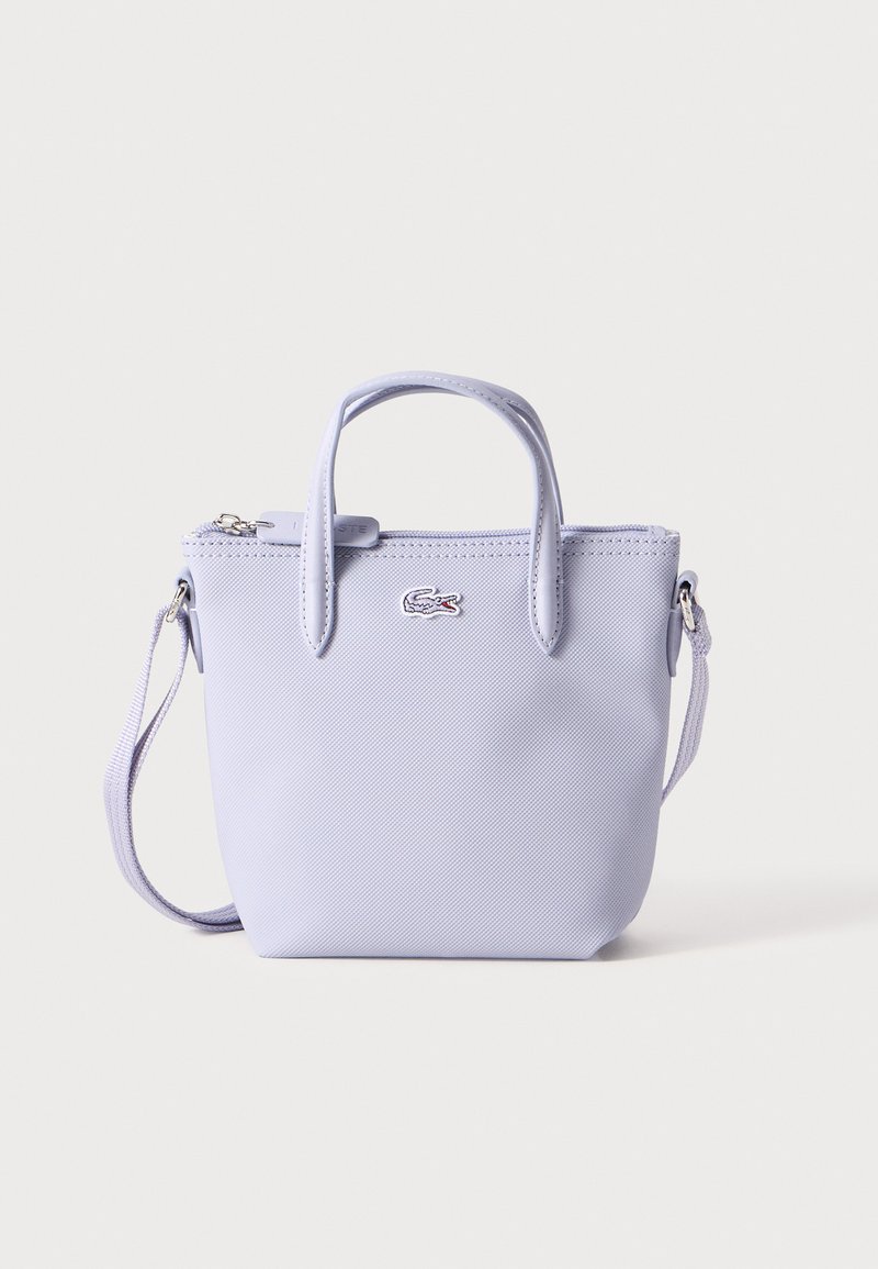 Fioletowa torebka z teksturowanym wykończeniem, podwójnymi uchwytami, odpinanym paskiem na ramię i zapięciem na zamek. Posiada mały akcent logo z przodu.