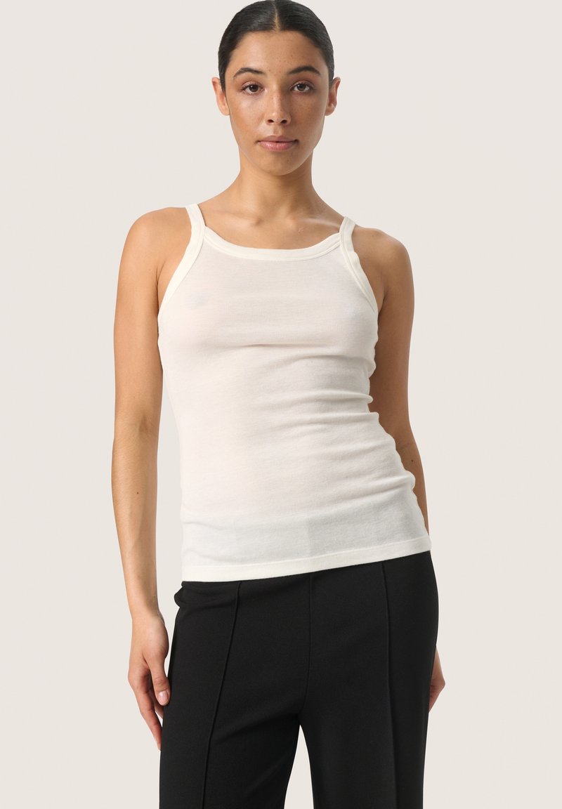 Top bianco aderente realizzato in tessuto leggero, con scollatura a barca e spalline sottili. Abbinato a pantaloni neri.