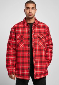 Red and black plaid flannel shirt with two chest pockets, button closure, and a soft texture. Long sleeves with buttoned cuffs.