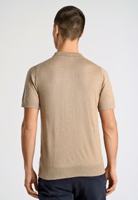 Beige kortärmad poloskjorta med klassisk krage, ribbad fåll och ärmslut. Slät textur med ett subtilt stickat mönster.
