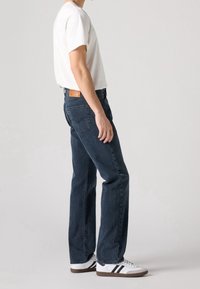 Mörkblå denimjeans med rak passform, med en läderlapp på baksidan, bärs med en vit t-shirt och vita sneakers med svarta ränder.