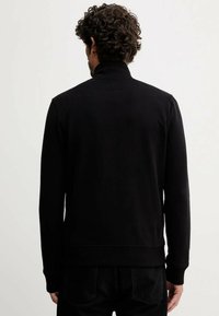 Maglione nero a girocollo con colletto alto. Realizzato in tessuto liscio, presenta una linea aderente e maniche lunghe con polsini a coste.