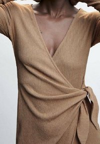 Robe enveloppante en maille texturée marron, avec un décolleté en V profondeur, des manches longues et un détail de nœud sur le côté à la taille.