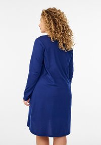 Vestido azul marino de manga larga con un ajuste relajado, tela suave, escote redondo y largo hasta la rodilla, con una textura lisa y sin patrones visibles.