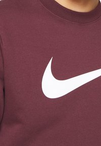 Maroon sweatshirt made of cotton, featuring a large white Nike swoosh logo on the front. Round neck and ribbed cuffs. Soft texture.