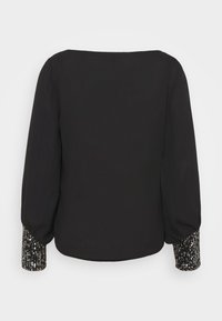 Blusa nera con maniche lunghe e polsini decorati con paillettes. Texture liscia, vestibilità comoda e scollatura a barca.