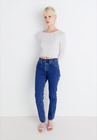 Ανοιχτό γκρι μακρυμάνικο ριμπ τοπ με cropped τελείωμα, σε συνδυασμό με ψηλόμεσα μπλε τζιν παντελόνια. Το μοντέλο φορά διαφανή σανδάλια με λουράκια.