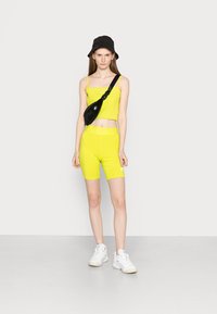 Sada neonově žlutého crop topu a šortek s texturovaným povrchem, spárovaná s černým kšiltem a černou crossbody taškou, a bílými teniskami.