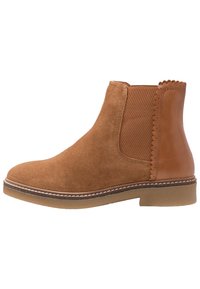 Botte Chelsea en daim marron avec panneau latéral élastique, détails en cuir festonnés sur le talon et semelle en caoutchouc basse.