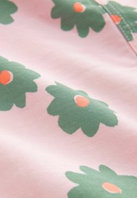 Tyg med rosa bakgrund som har stora gröna blommönster och orange mitt, vilket visar en slät textur och en lekfull design.