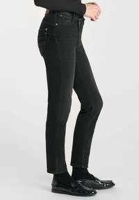 Jean skinny noir en denim avec taille haute, poches avant et arrière, et équipements en métal. Le matériau a une texture lisse.