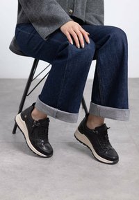 Zapatillas de cuero negro con suela beige, que presentan un detalle de cremallera y cierre de cordones. Combinadas con denim oscuro con dobladillos enrollados.