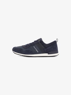 Marinblå sneaker i mocka och mesh, med en vit gummisula, platta snören och märkesdetalj på sidan. Rund tå och texturerade accenter.