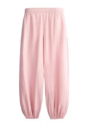 Femme portant un pantalon rose fluide à taille haute avec une ceinture élastique et des poches avant, assorti à un top court noir.
