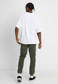 Hvit kortermet t-skjorte kombinert med olivengrønne, smale bukser. Svarte sneakers med hvite såler og svarte detaljer er brukt.