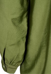 Långärmad olivgrön skjorta med samlad ärm och knapp, med en liten sidöppning nära ärmen.